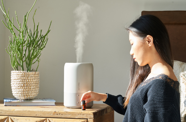 Woman adding essential oil to a white humidifier on a wooden side table