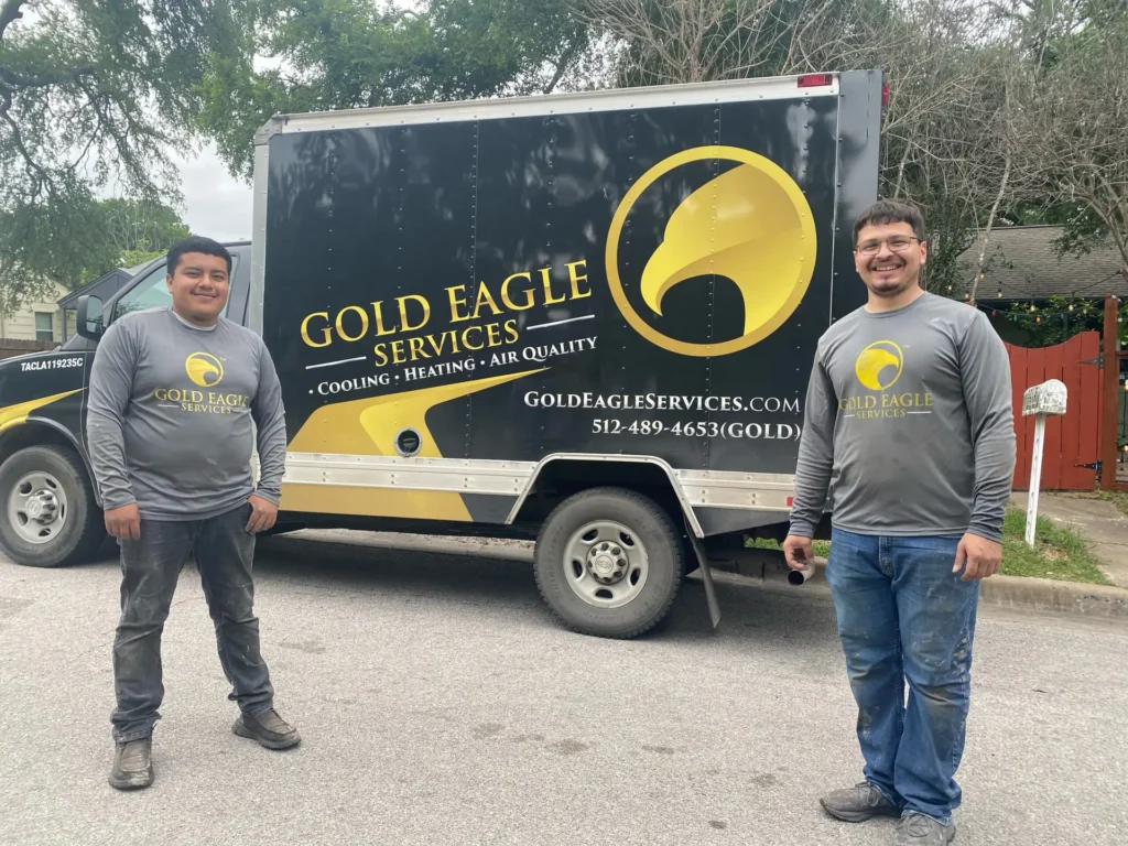 Two smiling technicians in gray Gold Eagle Services shirts stand beside a dark company truck with bold yellow eagle branding.