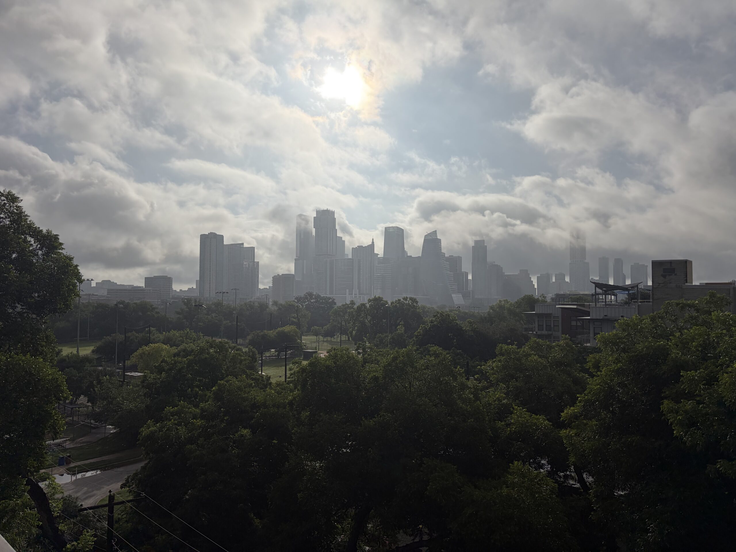 Downtown Austin skyline under cloudy skies above a green tree canopy