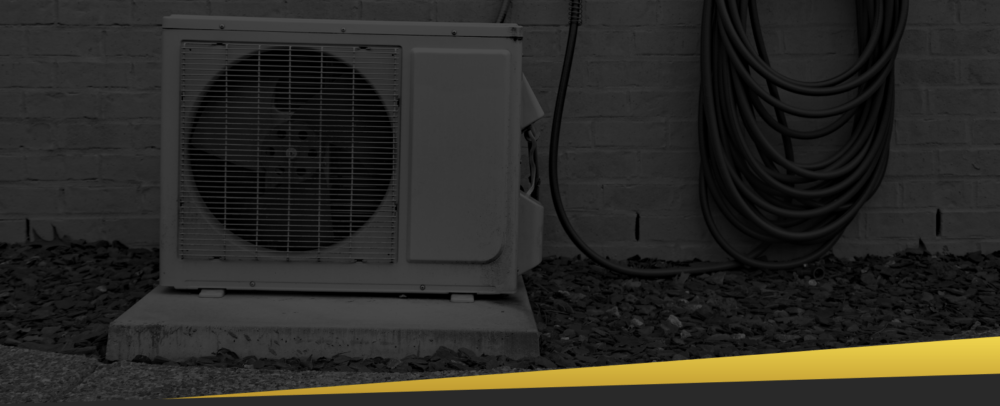 Outdoor air conditioning unit installed against a brick wall with a coiled hose nearby