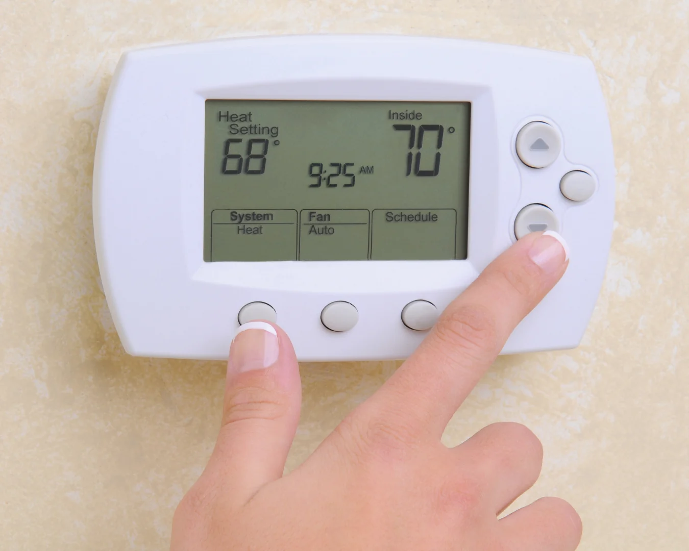 A hand presses a button on a white thermostat displaying a 68-degree heat setting and an indoor temperature of 70 degrees.