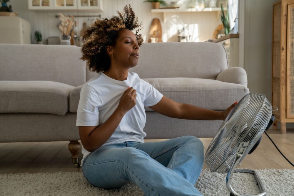 A woman sitting on the floor using a fan to cool herself in a cozy living room
