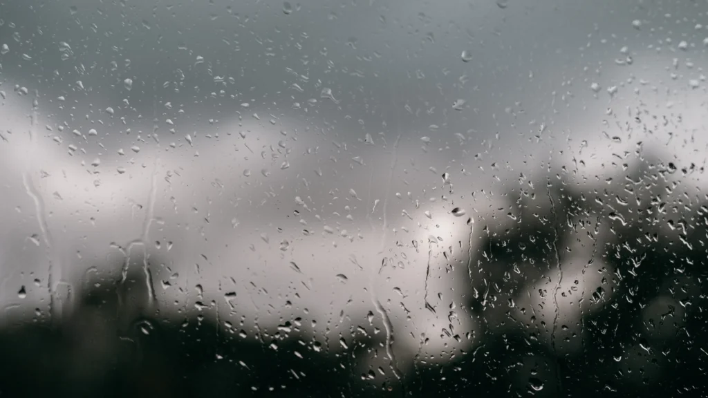 Clear droplets and condensation streaks cover a window, with a blurred dark exterior beyond the glass, evoking Austin's humid summer air.