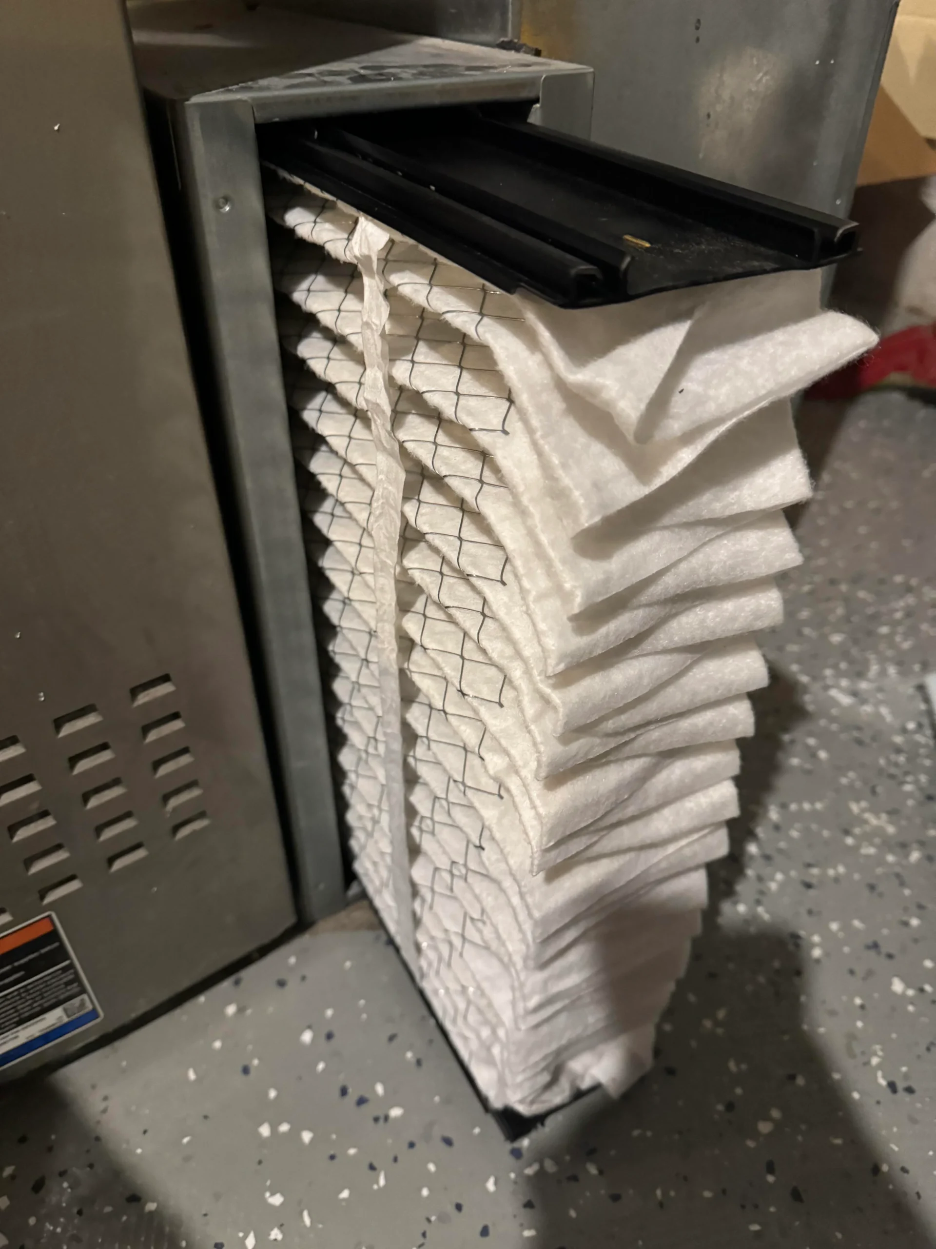 Thick pleated media air filter pulled out of an Aprilaire filter cabinet