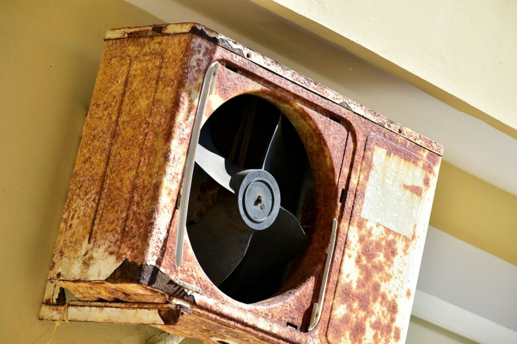 Badly rusted wall-mounted air conditioner unit with a missing fan guard