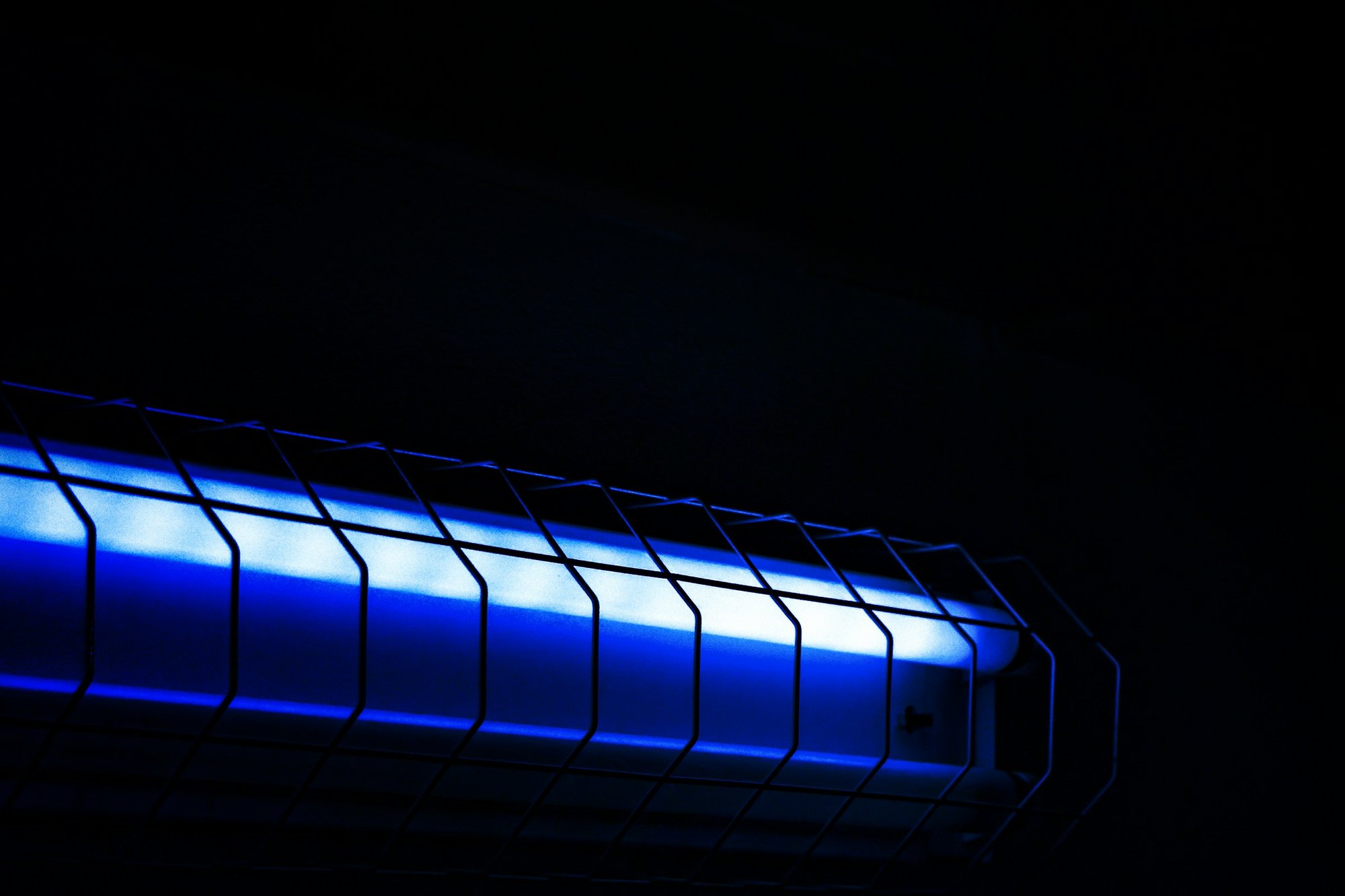 Blue-violet ultraviolet tube lamp glowing in a dark space