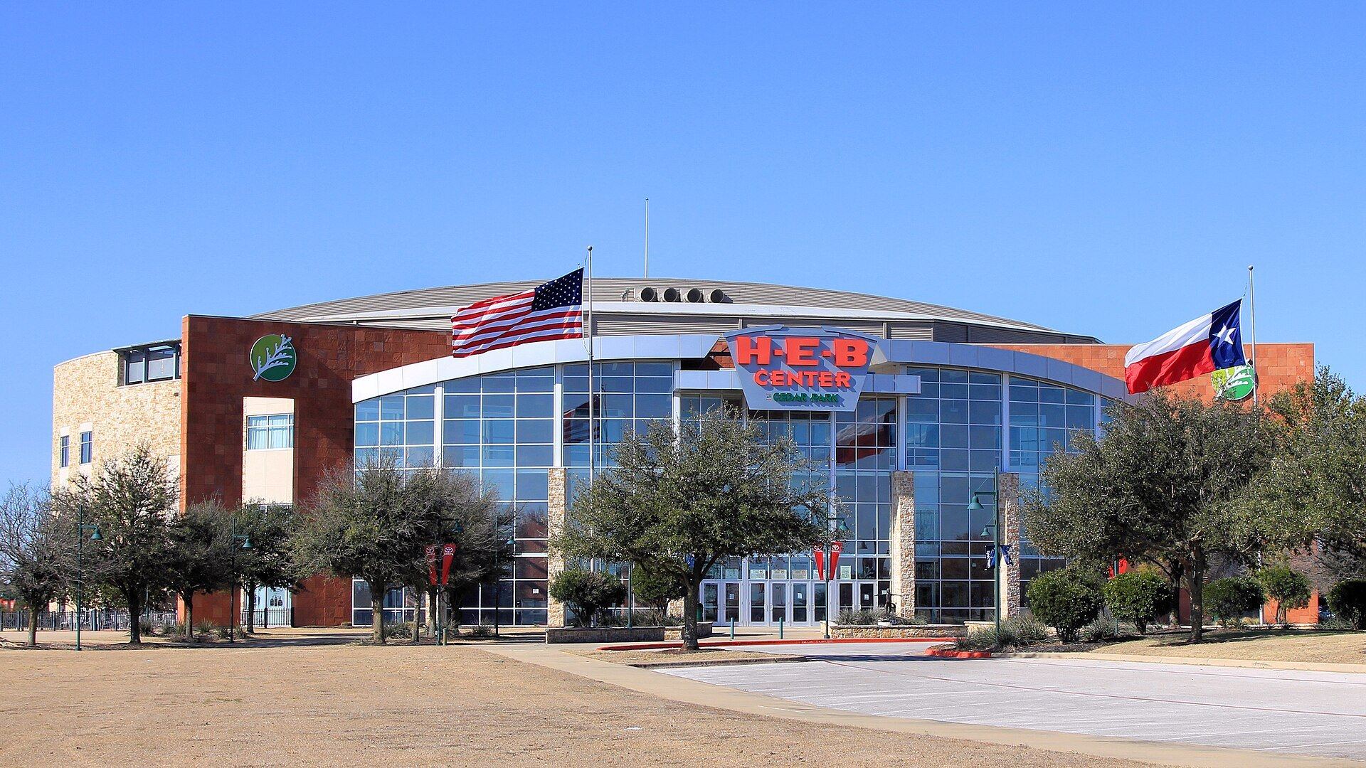 H-E-B Center at Cedar Park arena with American and Texas flags under a blue sky in Cedar Park, Texas
