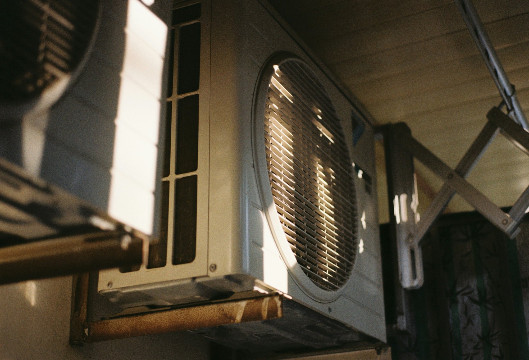 Close-up of an outdoor air conditioner fan grille lit by afternoon sun
