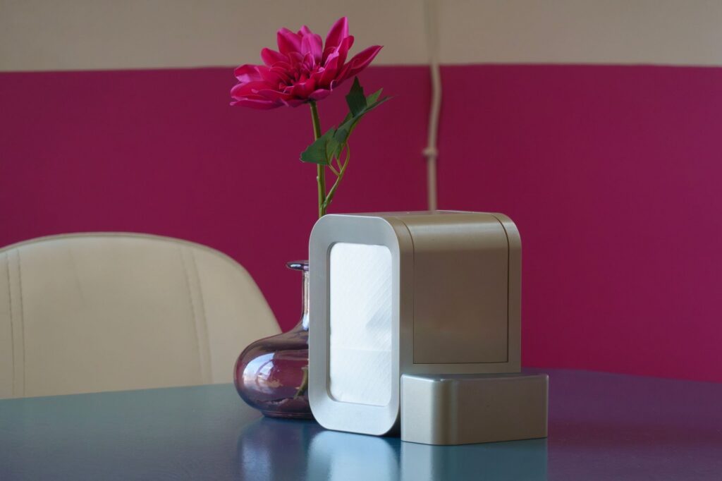 Compact air purifier on a table beside a vase with a pink flower