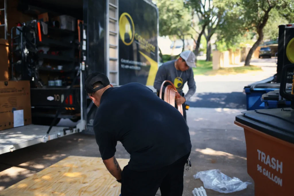 Two Gold Eagle Services technicians handle tools beside an open service truck, with a coiled copper-colored line and gear visible.