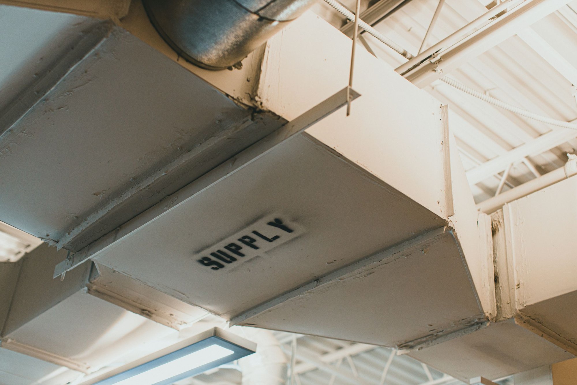 Exposed sheet-metal supply air duct labeled SUPPLY on a ceiling