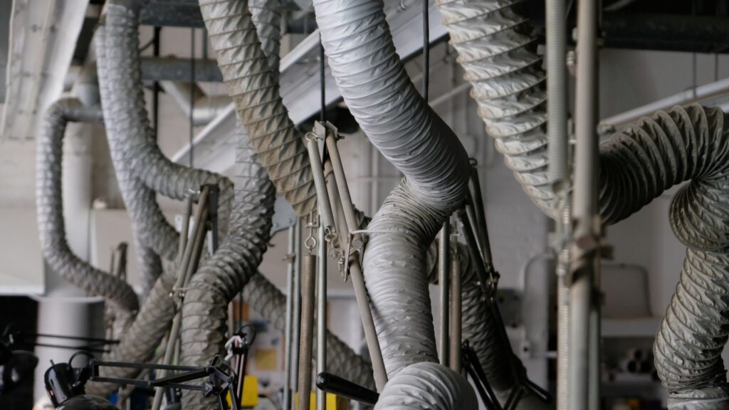 Flexible gray air ducts hanging from a ceiling in a mechanical space