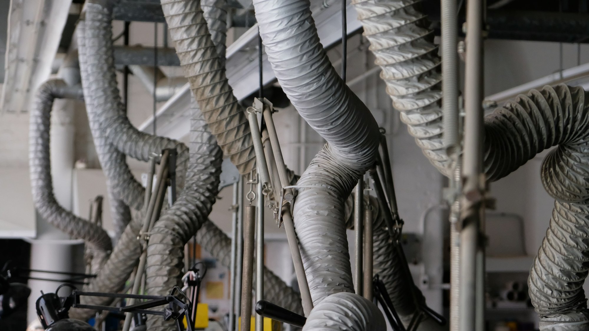 Flexible gray air ducts hanging from a ceiling in a mechanical space