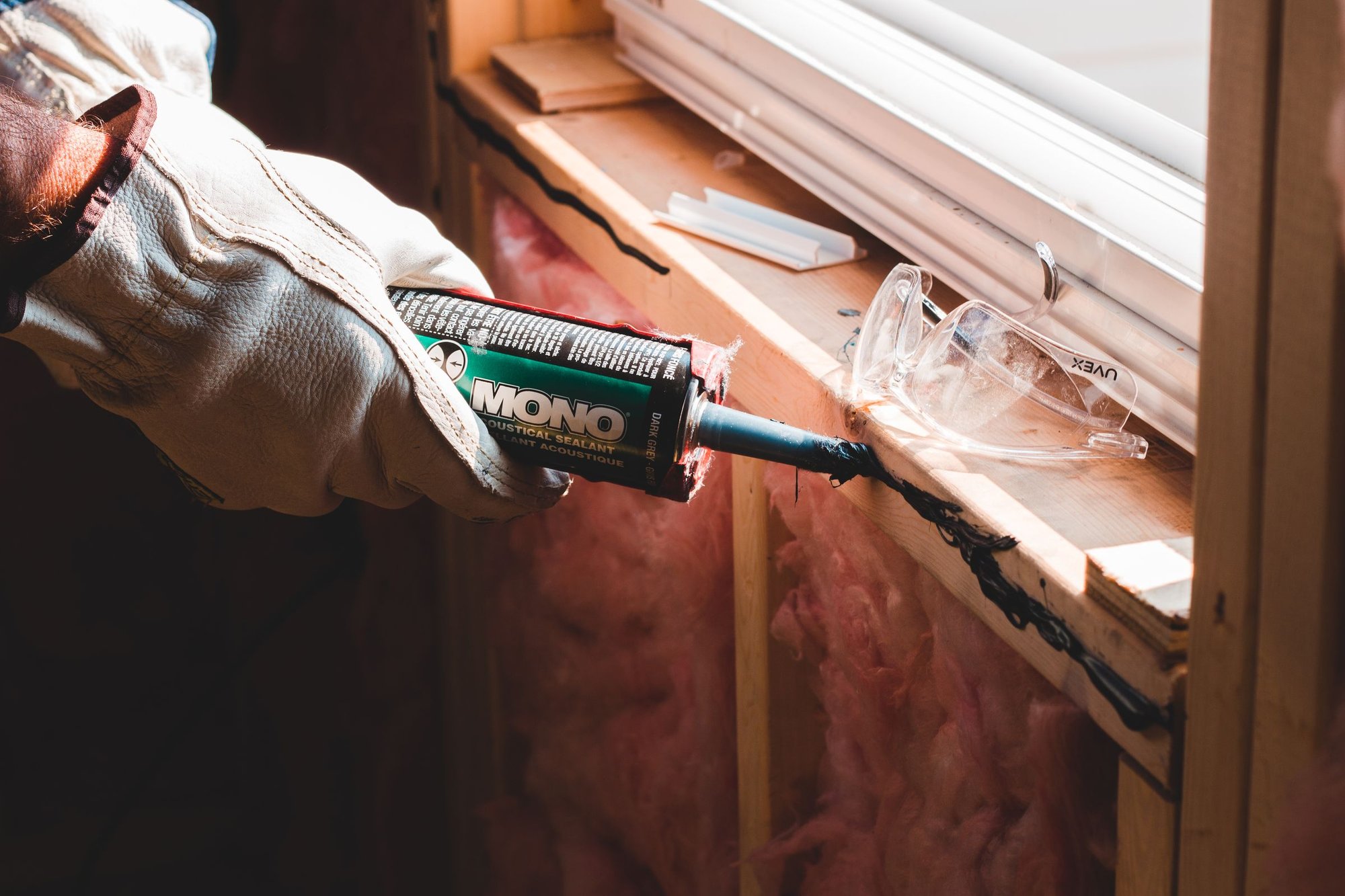 Gloved hand applying caulk to seal a gap around a window frame