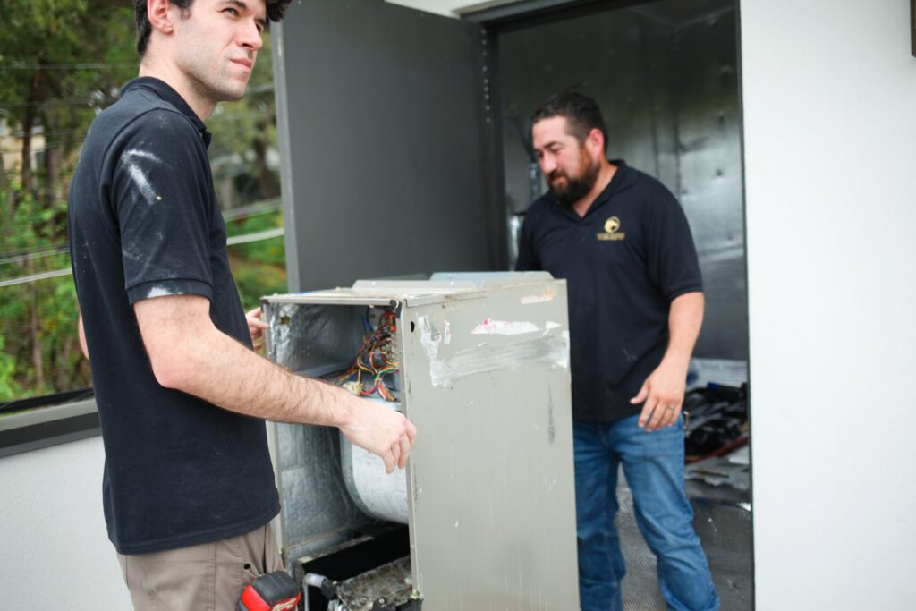 Two Gold Eagle technicians working on an air handler in an indoor equipment closet