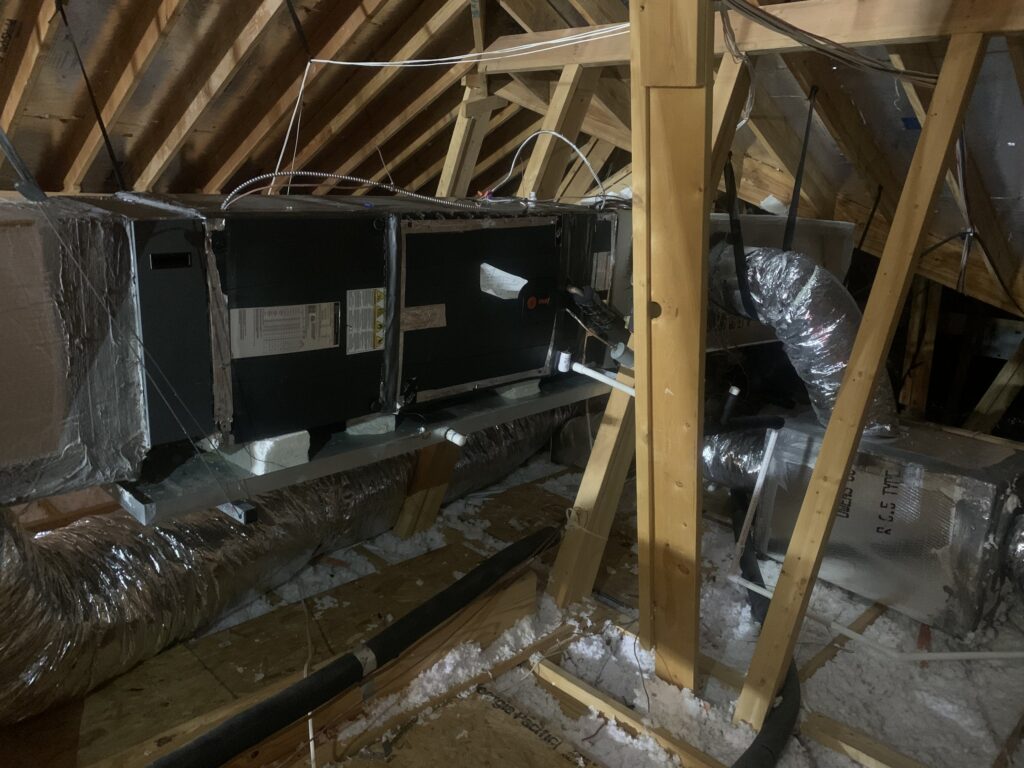 A horizontal air handler sitting in a metal secondary drain pan on an attic platform, with foil-wrapped plenums at each end and flex duct below