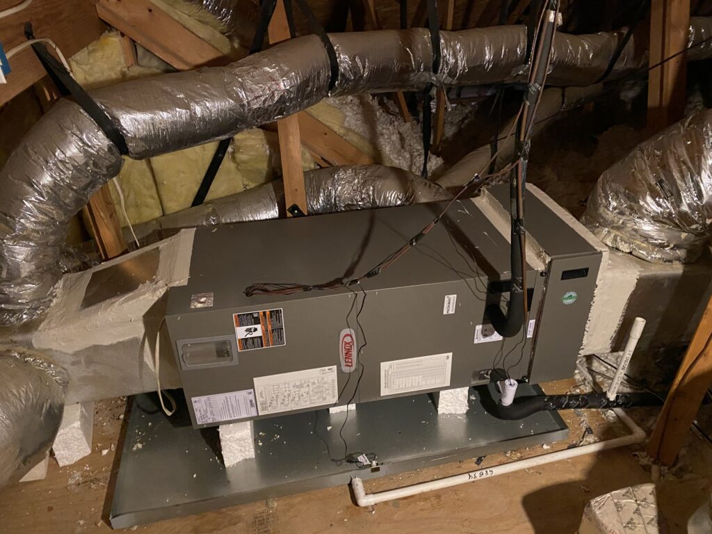 A single horizontal air handler on its secondary drain pan in an Austin attic, with ductboard plenums at each end and flex duct runs leaving them
