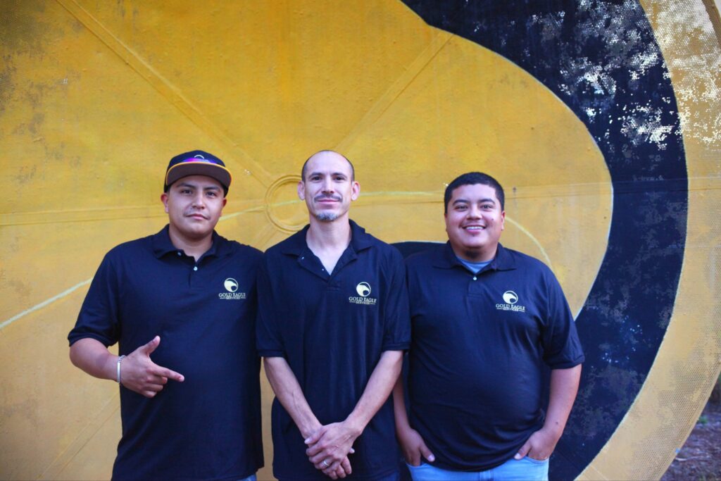 Three Gold Eagle installers in navy company polos in front of the gold eagle logo wall