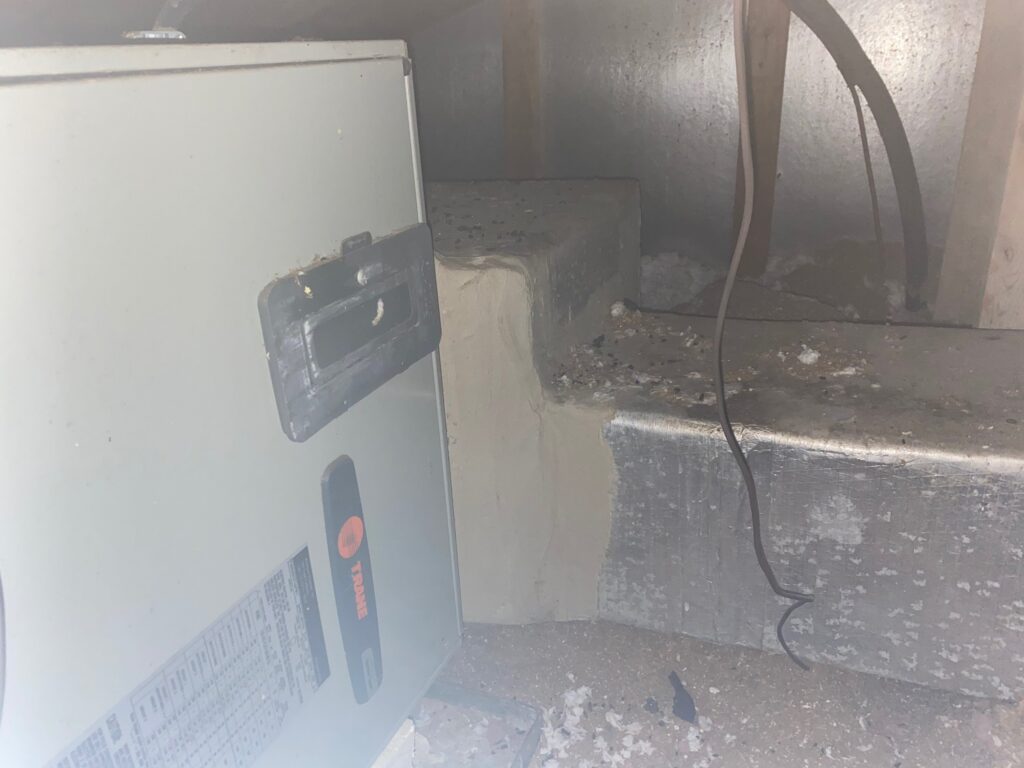 Older indoor unit beside a dusty foil-faced ductboard plenum in an attic