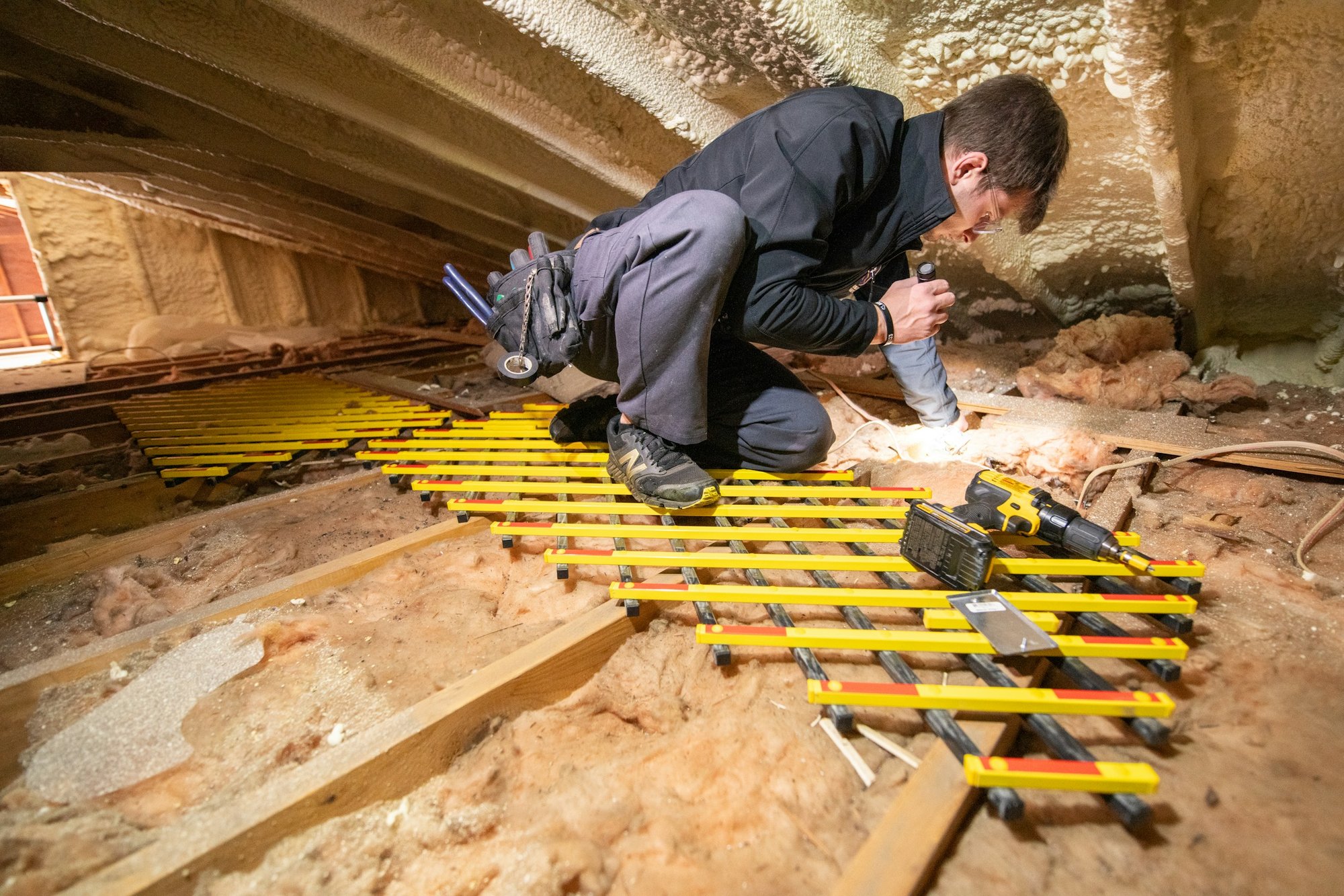 Installer working in an attic over insulation and spray foam