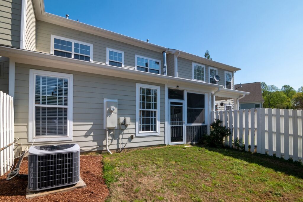 Outdoor central AC condenser beside a home with a fenced backyard