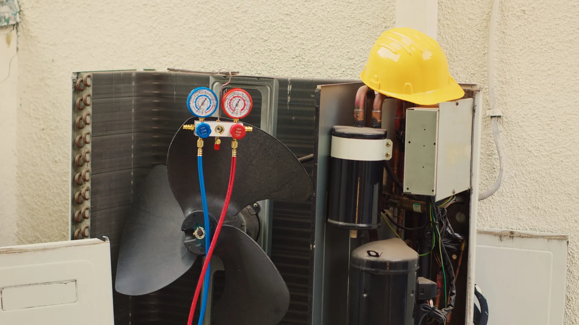 An open HVAC cabinet exposes a large blower wheel, copper tubing, electrical controls, and red and blue service gauge hoses.