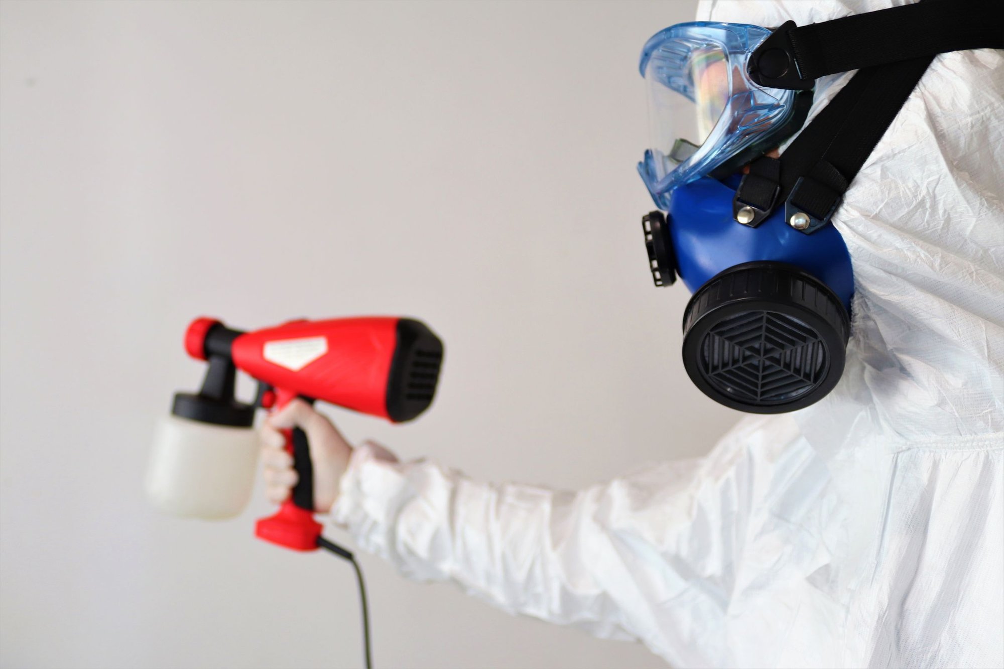 Person in protective suit and respirator holding a handheld disinfectant sprayer
