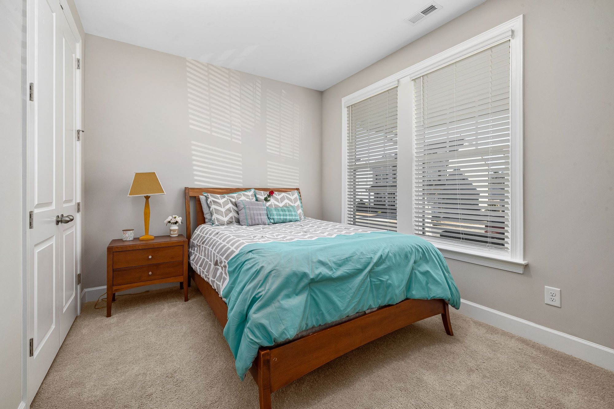 Quiet, cozy bedroom with a made bed, wood furniture and window blinds