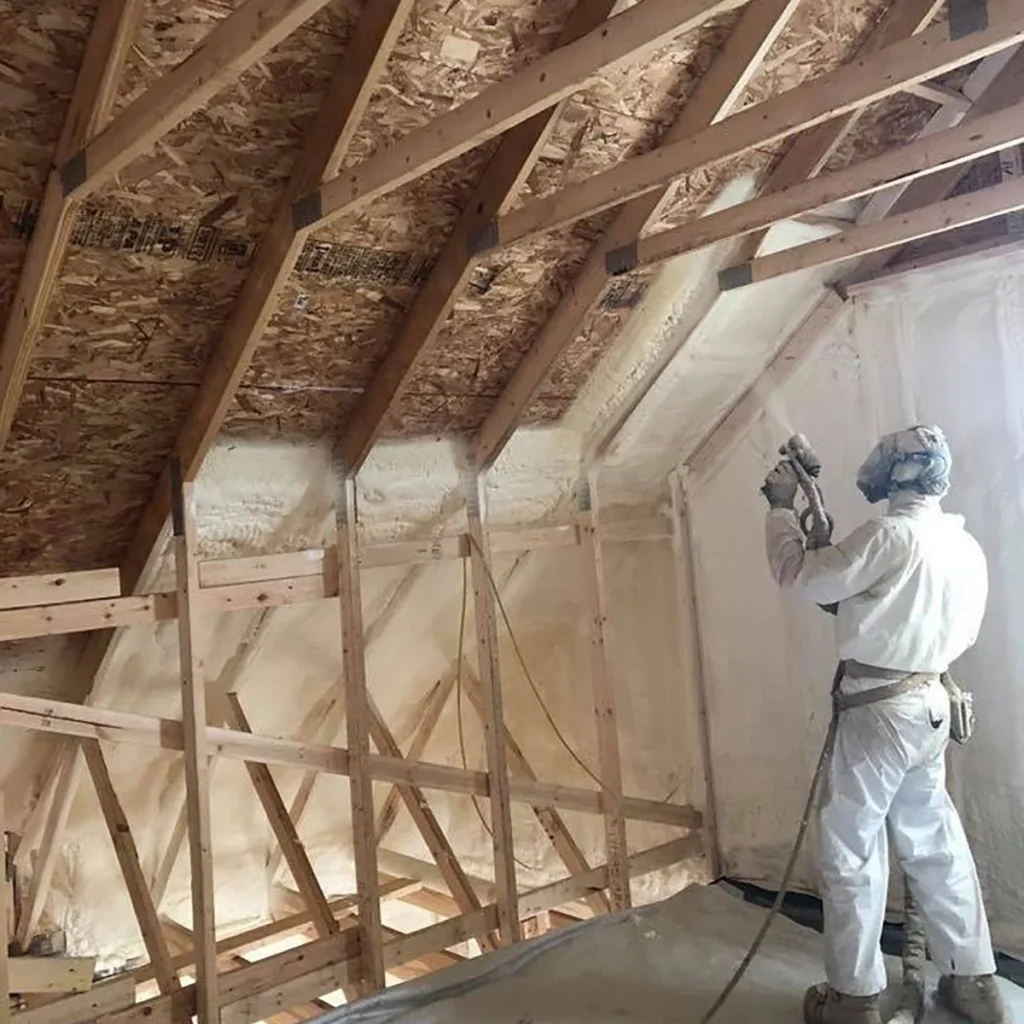 Installer in protective gear spraying foam insulation on an attic roof deck