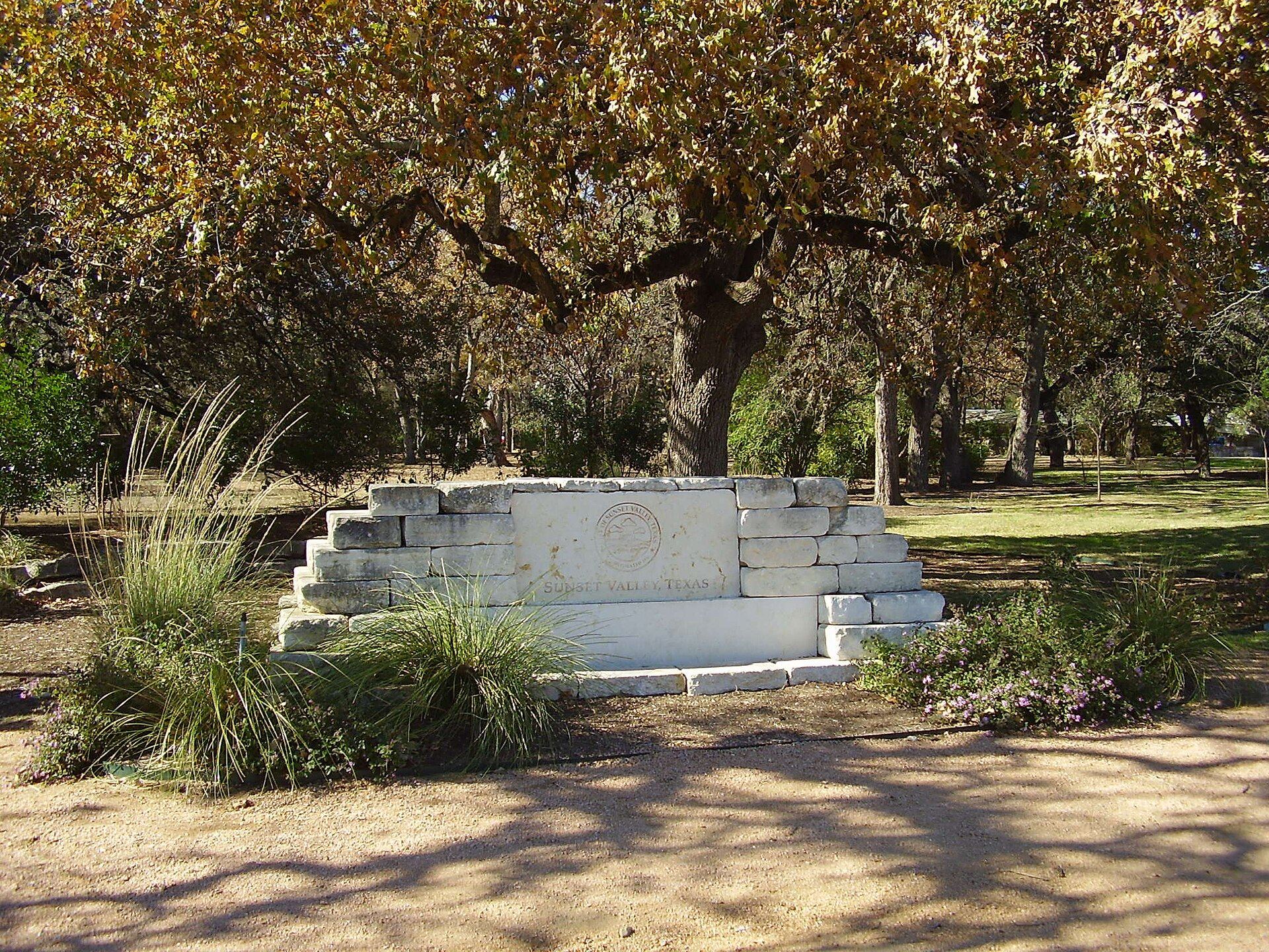 Limestone city monument under large oak trees in Sunset Valley, Texas
