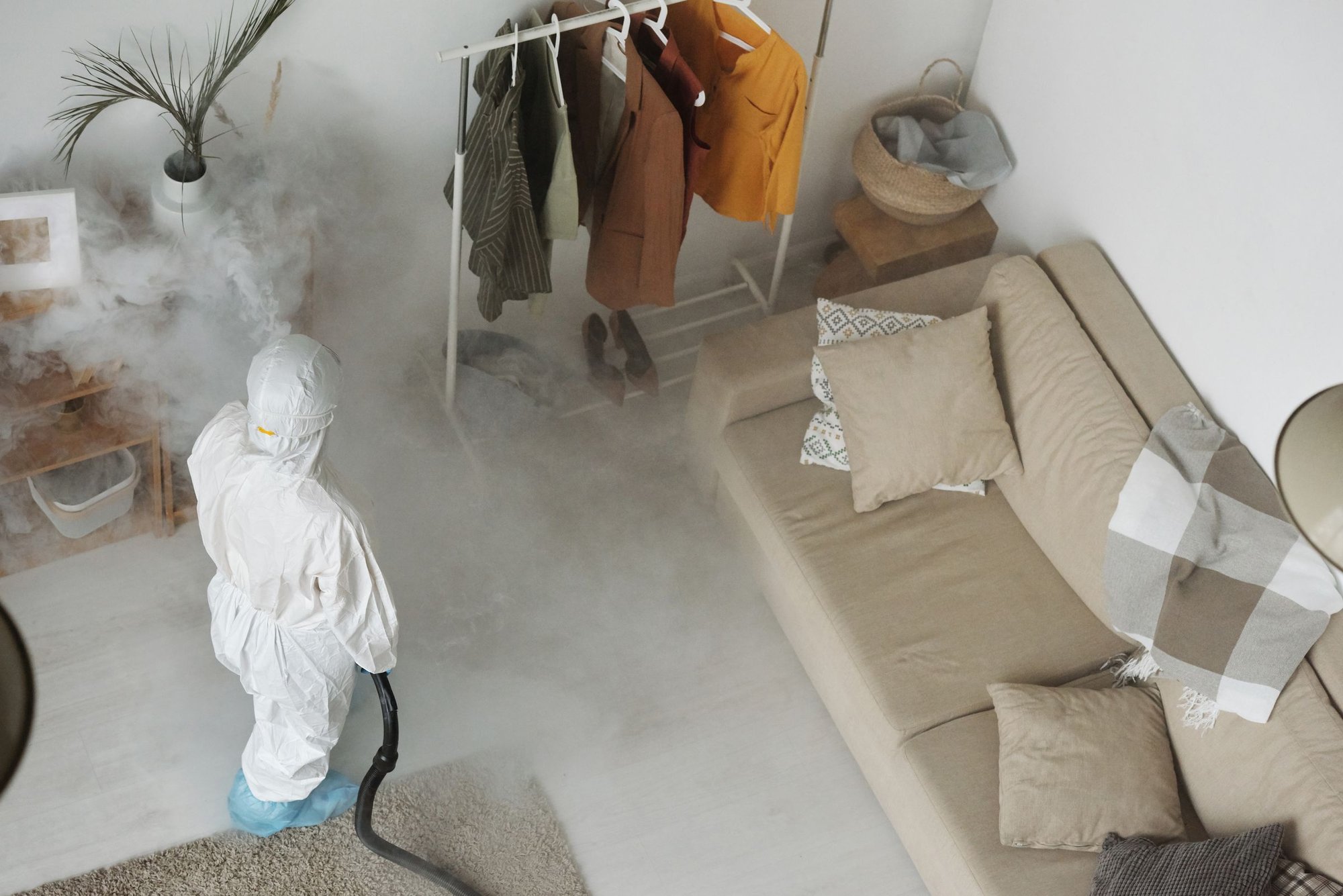 Technician in protective gear misting a living room with a fogging machine