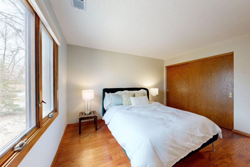 Tidy guest bedroom with a white bed, wood floors and a large window