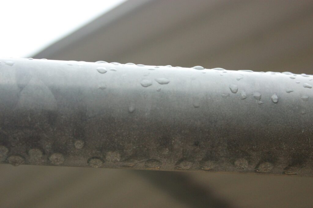 Water droplets beading on a metal pipe, like condensation on an air conditioner refrigerant line