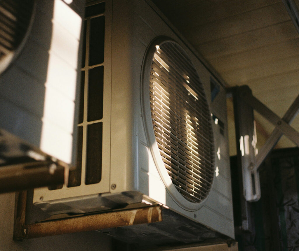 A close view of a gray outdoor air conditioning unit shows its curved black grille, side panels, and metal mounting supports.