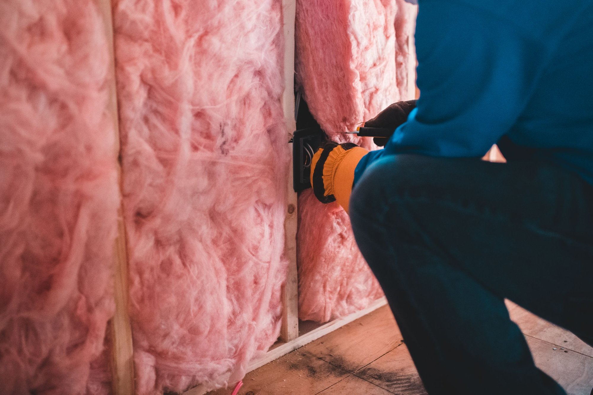 Worker installing pink fiberglass batt insulation between wall studs